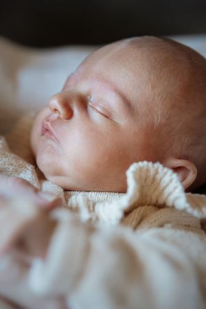 Peaceful newborn baby sleeping soundly wrapped in a soft cream knit blanket with eyes closed.