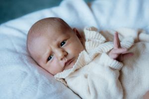 Newborn baby in cream knit outfit lying on white blanket, looking up with wide eyes.