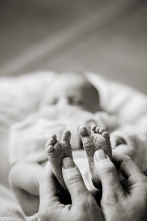 Black and white photo of an adult gently holding tiny newborn baby feet in their hands.