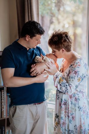 A couple tenderly kisses their newborn baby by a sunlit window in a cozy home.