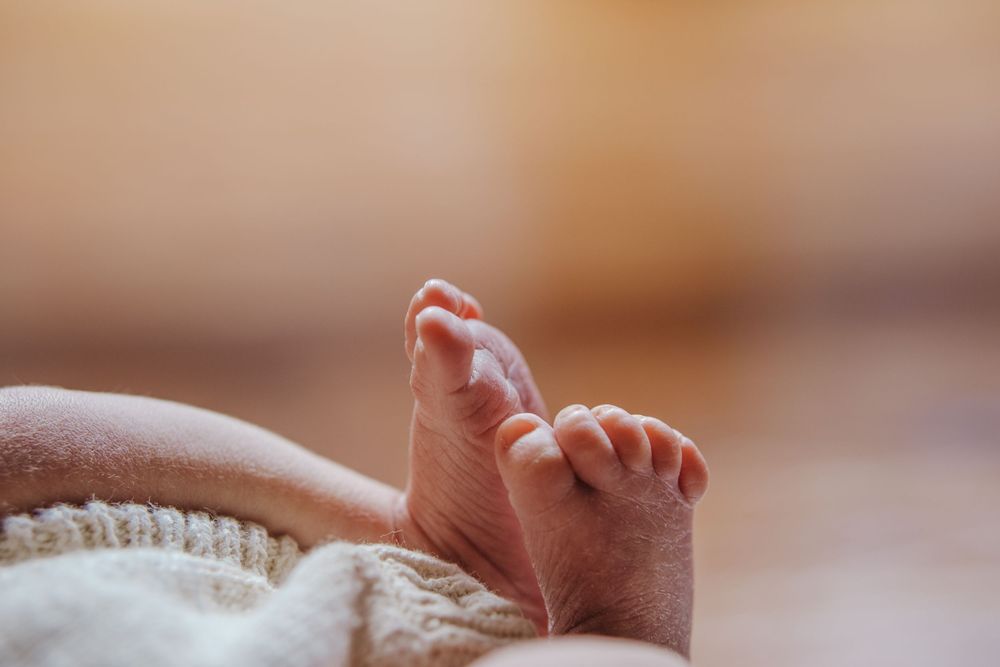 Close-up of newborn baby tiny feet wrapped in a soft white knit blanket with warm bokeh background during in home photoshoot in Castle Hill.