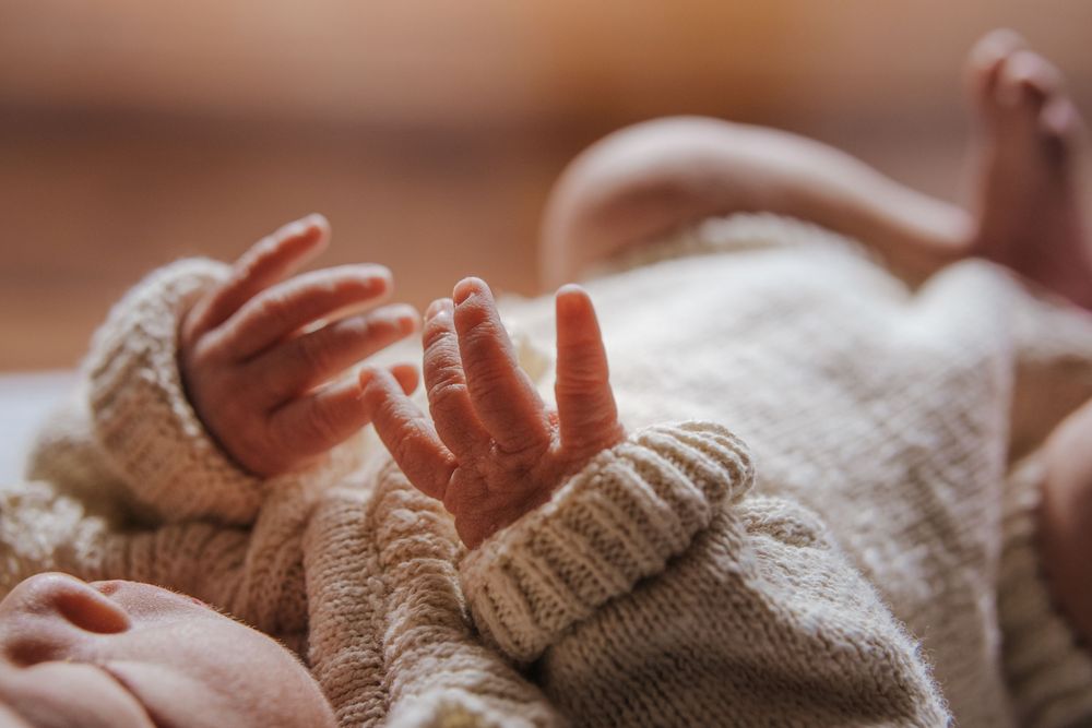 Close-up of a newborn baby's tiny hands and feet in a cozy knit sweater, capturing delicate infant details.
