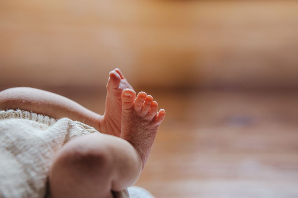 Close-up of adorable newborn baby feet wrapped in a soft white blanket with warm bokeh background.