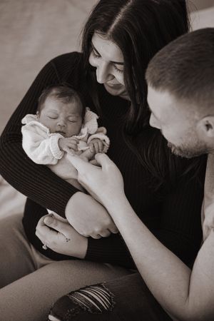 Black and white photo of new parents lovingly cradling their sleeping newborn baby together at home in Castle Hill.