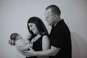 Black and white portrait of new parents smiling down at their swaddled newborn baby.