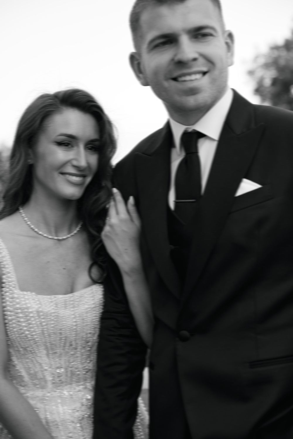 Smiling bride and groom pose together in black and white wedding portrait, bride wearing pearl necklace and beaded dress.