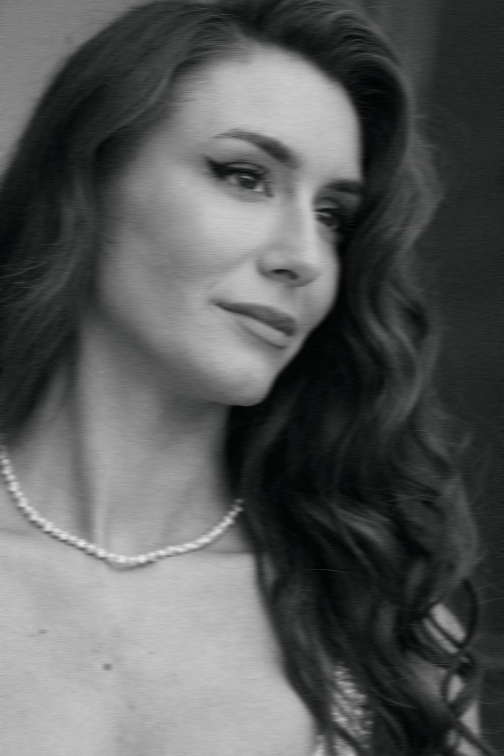 Close-up black and white portrait of bride with wavy hair wearing a delicate pearl necklace.