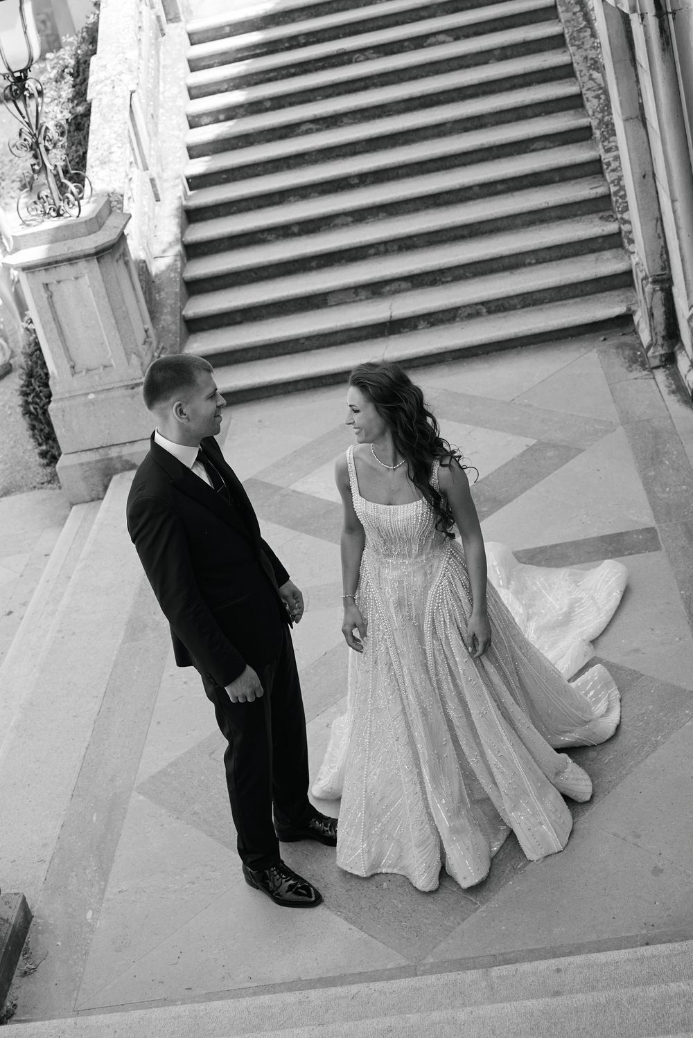 Black and white photo of bride and groom standing on ornate marble steps at elegant wedding venue.