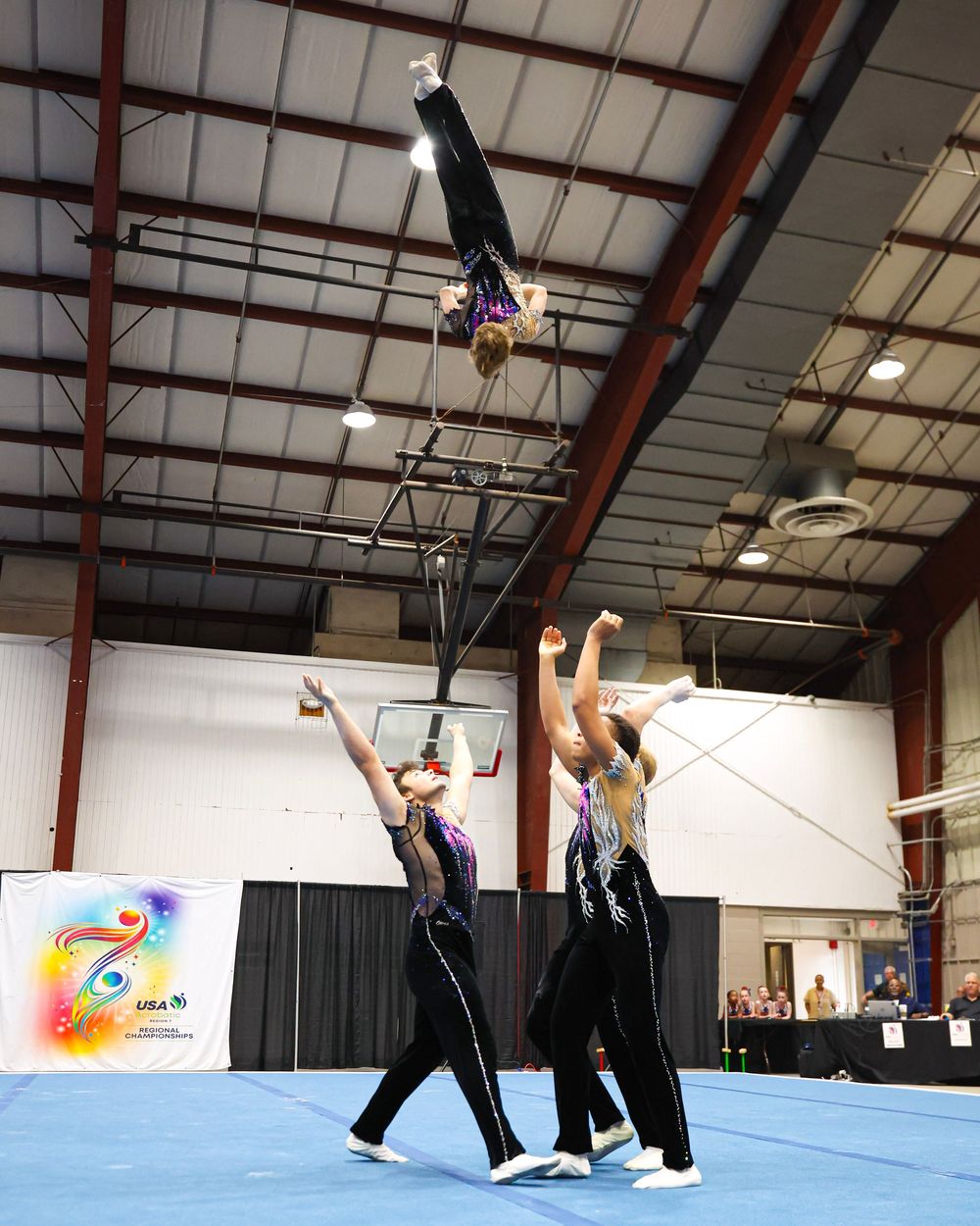 Acrobatic gymnasts perform a stunning balance routine indoors, with one athlete lifted high in an inverted position.