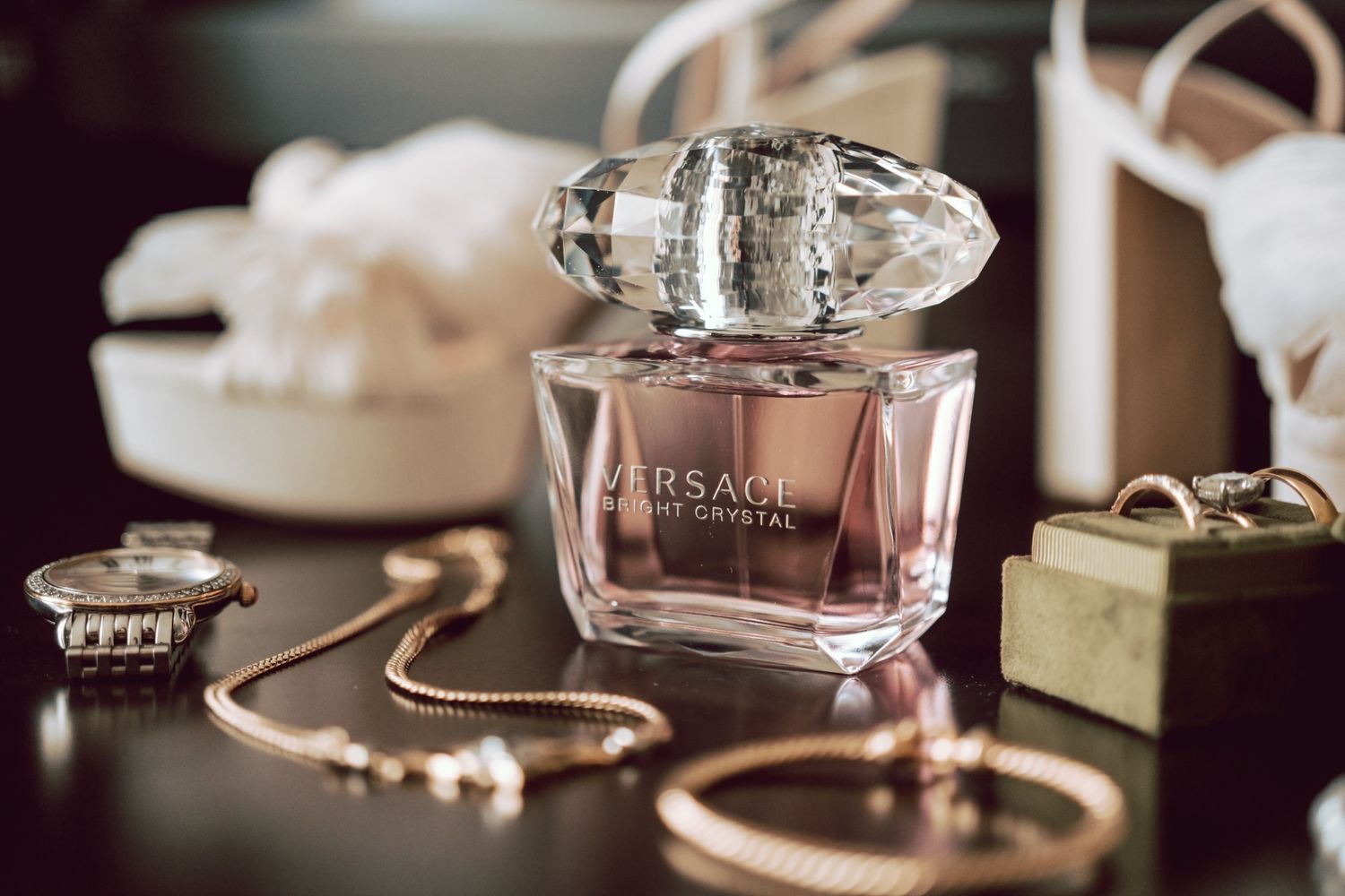Versace Bright Crystal perfume bottle with gold jewelry and accessories on a dark reflective surface.