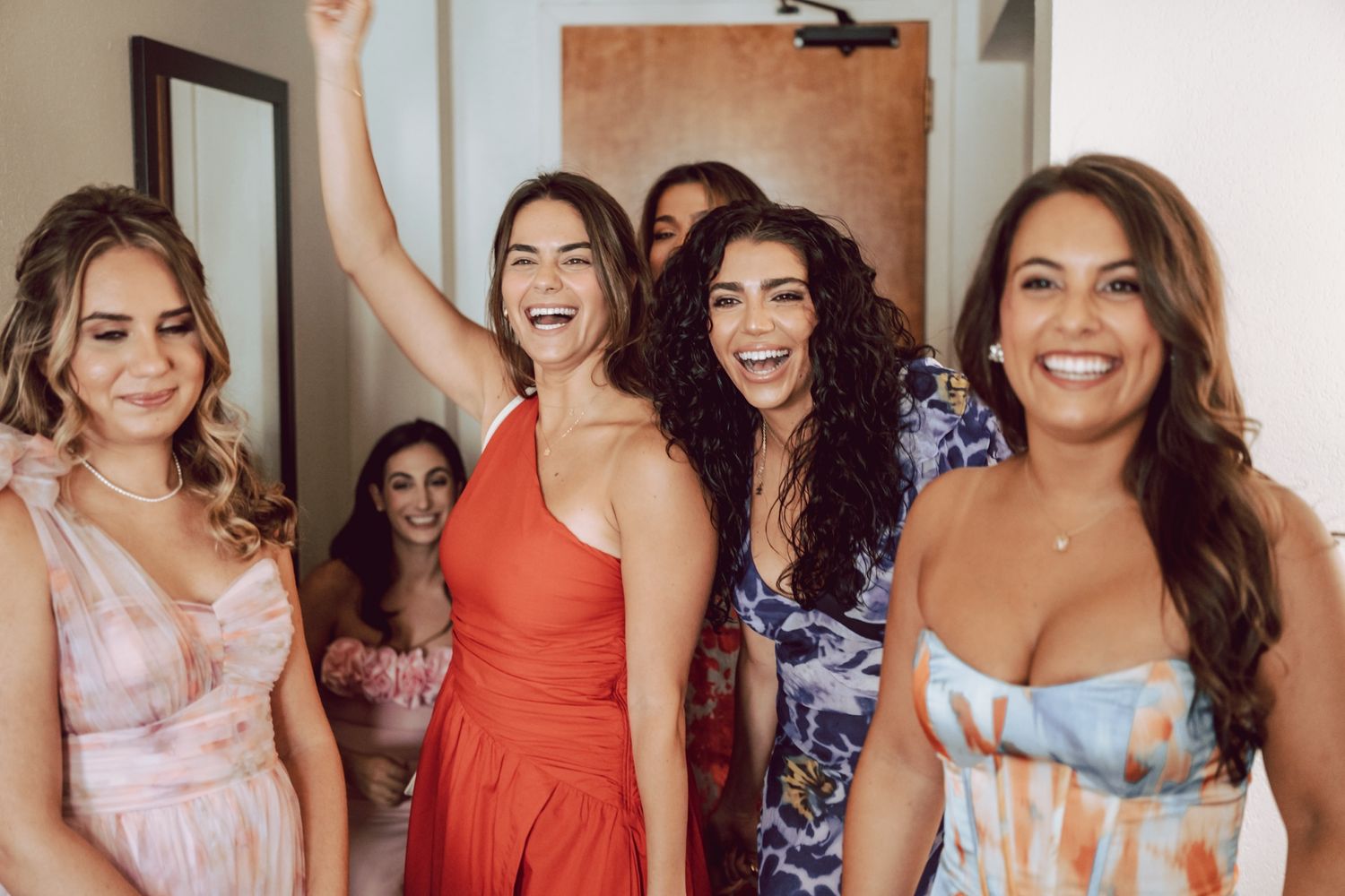 Excited bridesmaids in colorful dresses celebrate together while getting ready for a wedding.