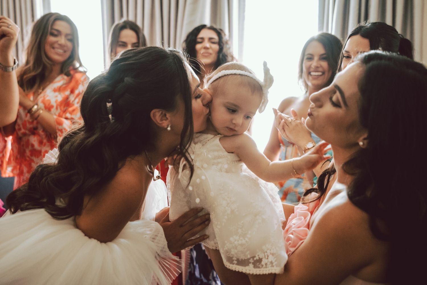 Bridesmaids and guests gathered around an adorable baby flower girl in a white lace dress.