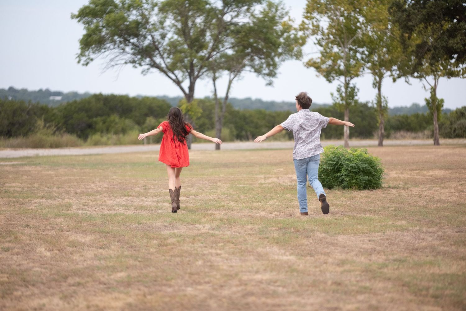 Couple running freely through open grassy field with arms outstretched, trees in background in Belton Texas