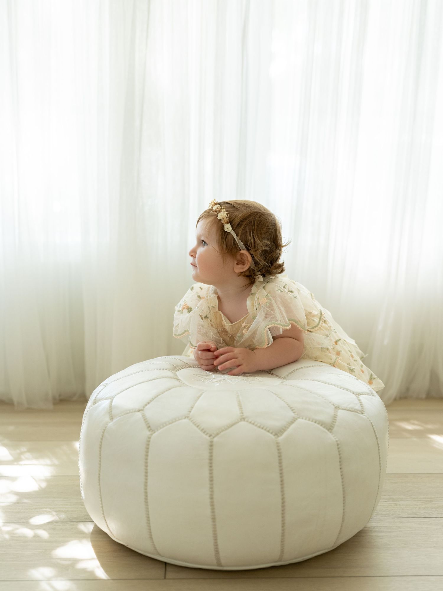 Adorable baby girl in floral dress and flower headband smiling with bright blue eyes.