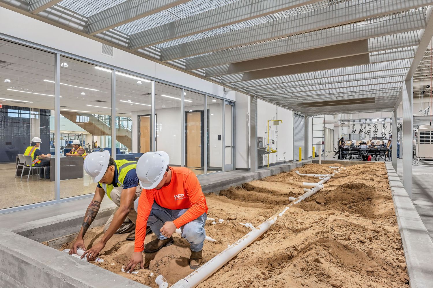 Construction workers installing underground pipes inside a modern building interior.