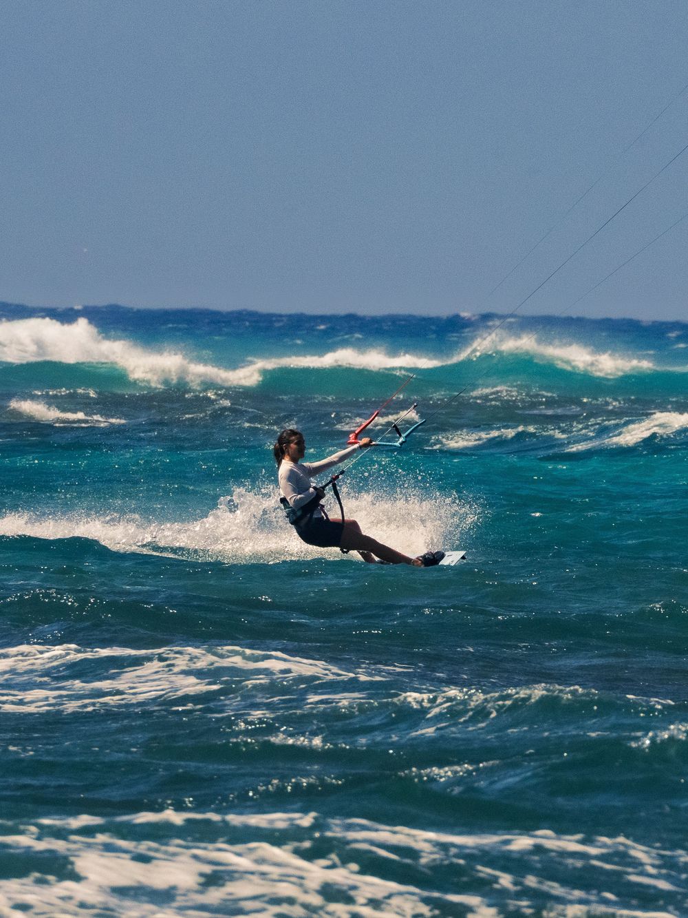 A kitesurfer leans back on the control bar riding a board across choppy turquoise water at Waikiki, spray flying and waves breaking behind.