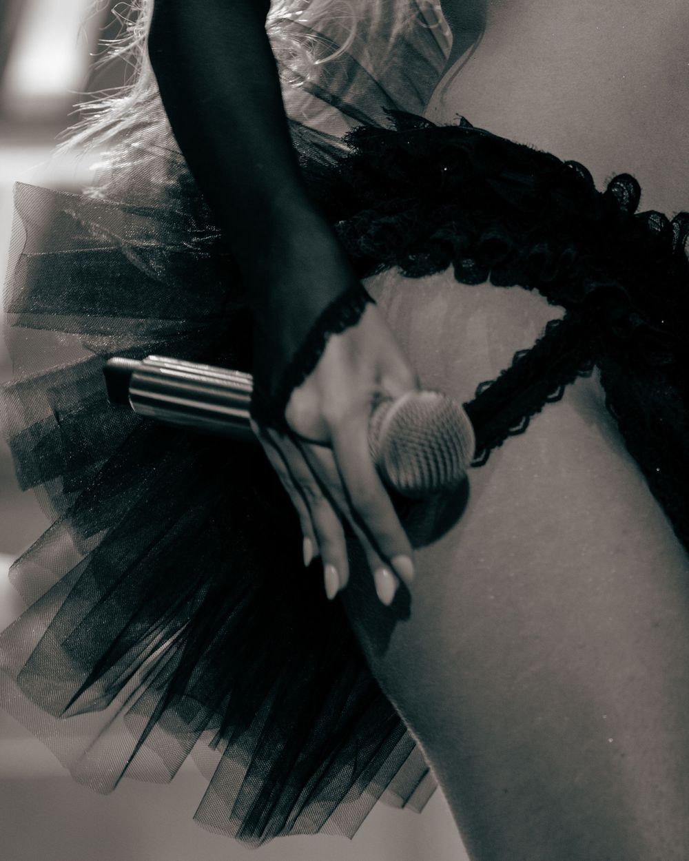 Black tutu skirt with lace waistband and silver accessory held by a dancer's hand in monochrome.