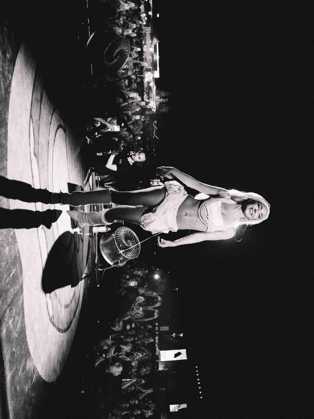 Black and white photo of a performer on stage with crowd and bright lights in the background.