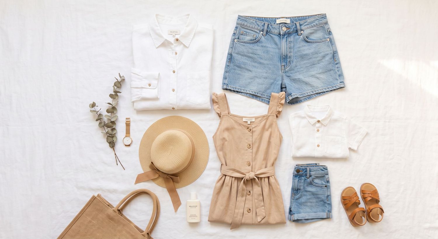 Flatlay of summer outfit with white shirt, denim shorts, tan top, straw hat, sandals, and woven bag on white background.