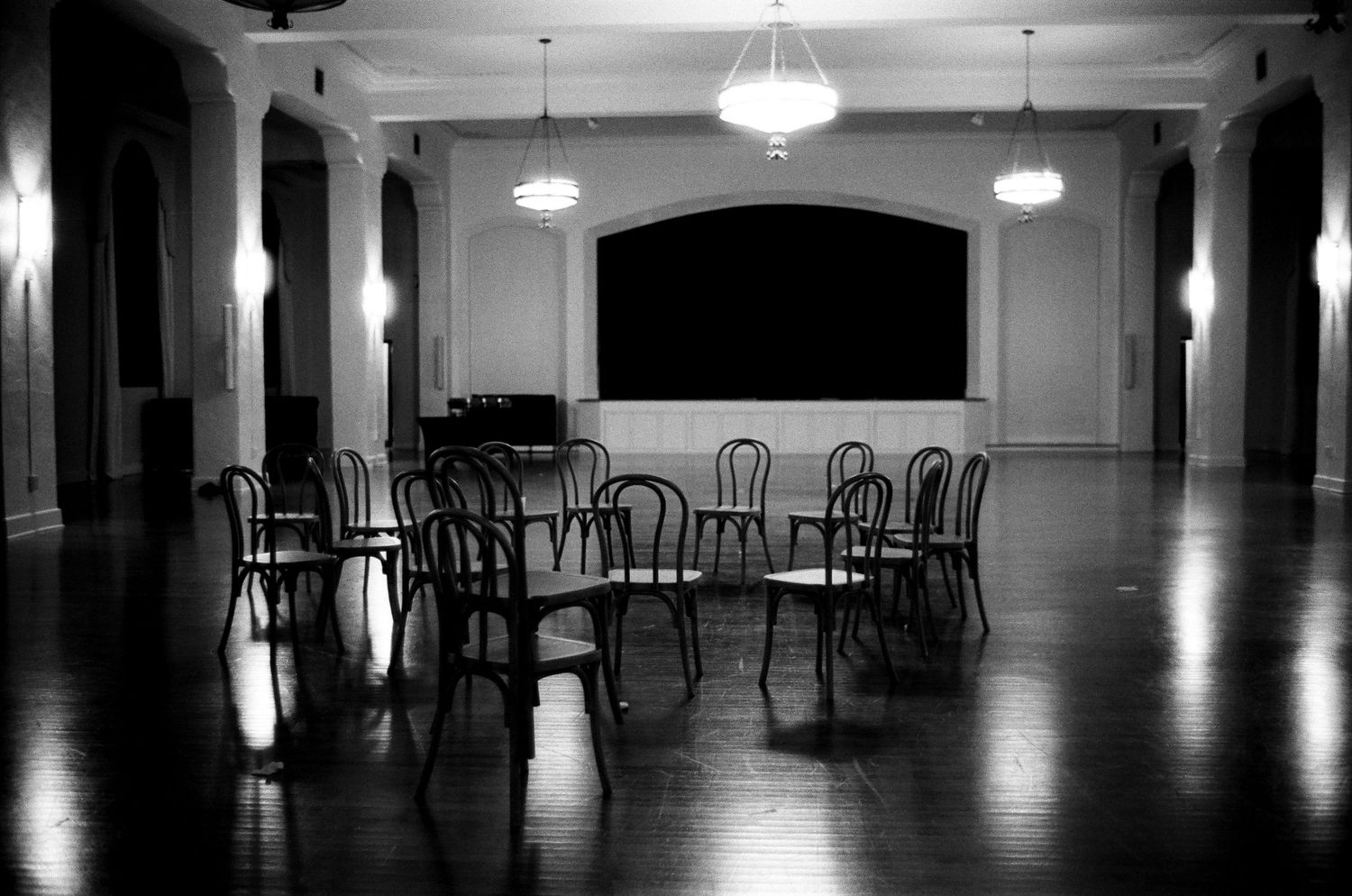 Black and white photo of empty chairs arranged in a circle on a hardwood floor in an elegant ballroom.
