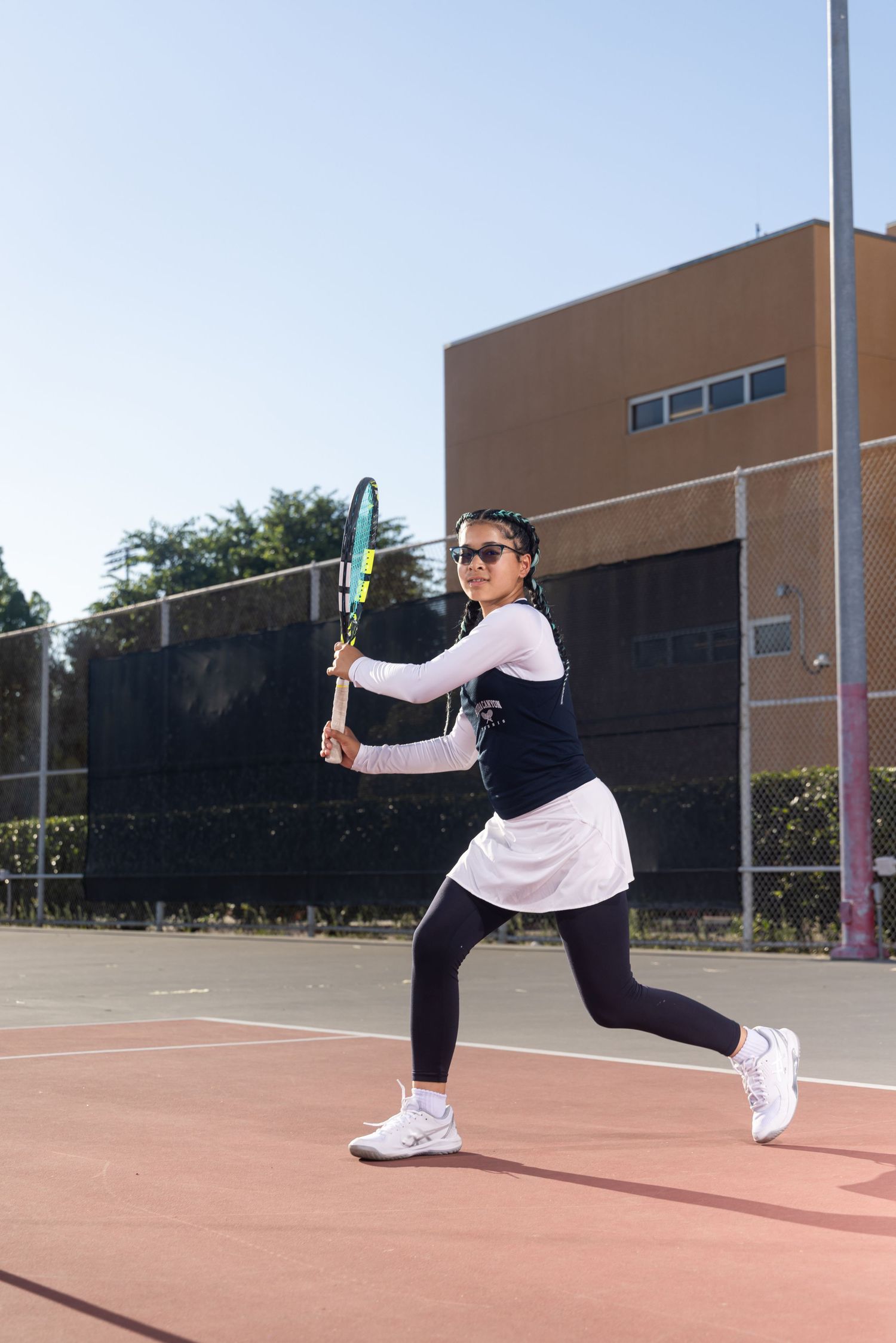 Woman in tennis outfit playing tennis on an outdoor court, mid-swing with a racket on a sunny day.