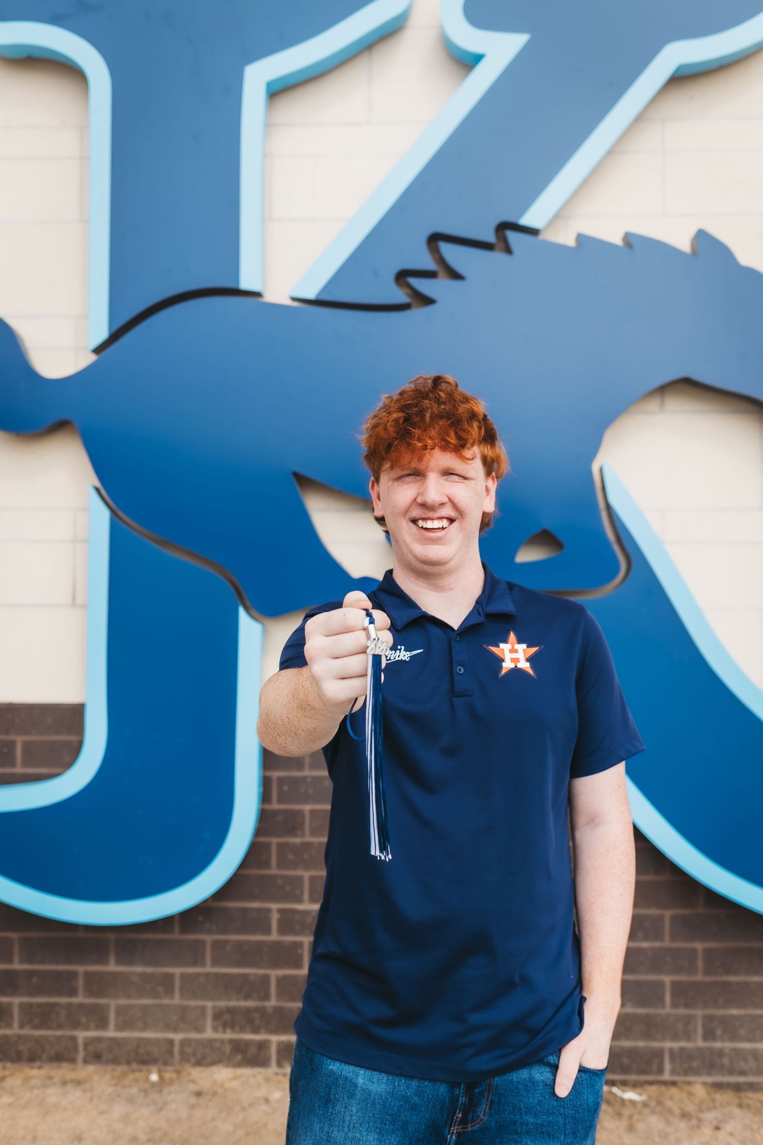 Smiling redhead teen holding keys in front of blue letter K mascot mural wearing Houston Astros polo shirt.