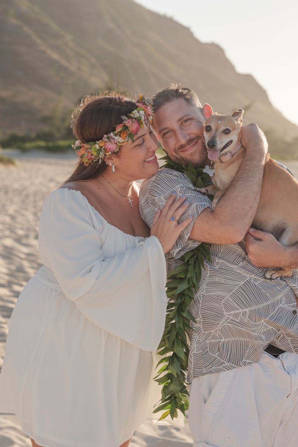 Bride and groom holding their dog during a North Shore Oahu beach wedding photography session with mountain views in the background.