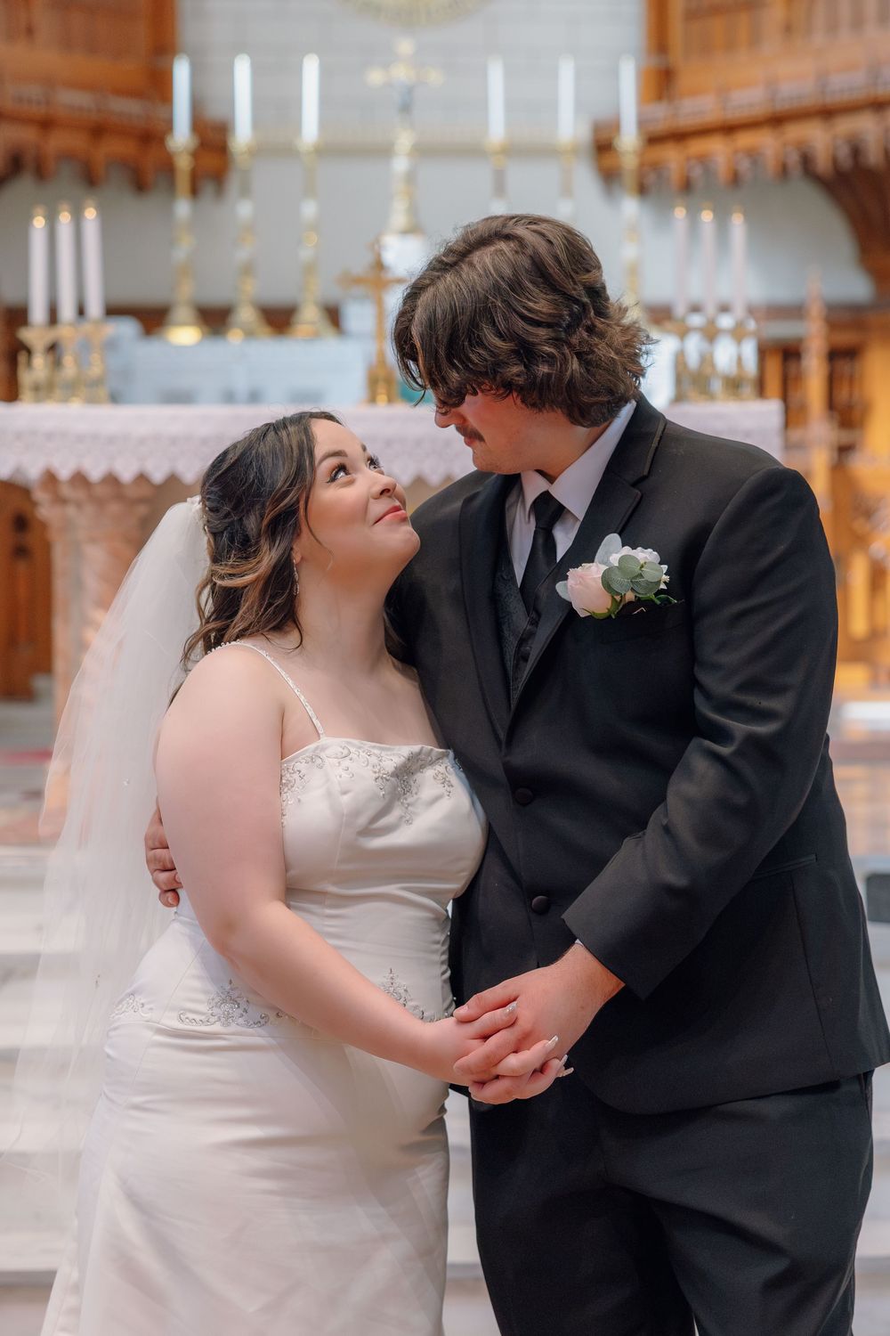 Bride in white gown and groom in black suit share romantic moment inside elegant church after wedding.