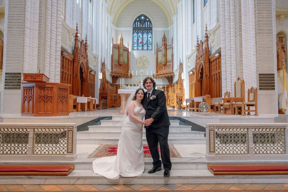 Bride and groom posing together at the altar of an elegant white church with wooden organ pipes.