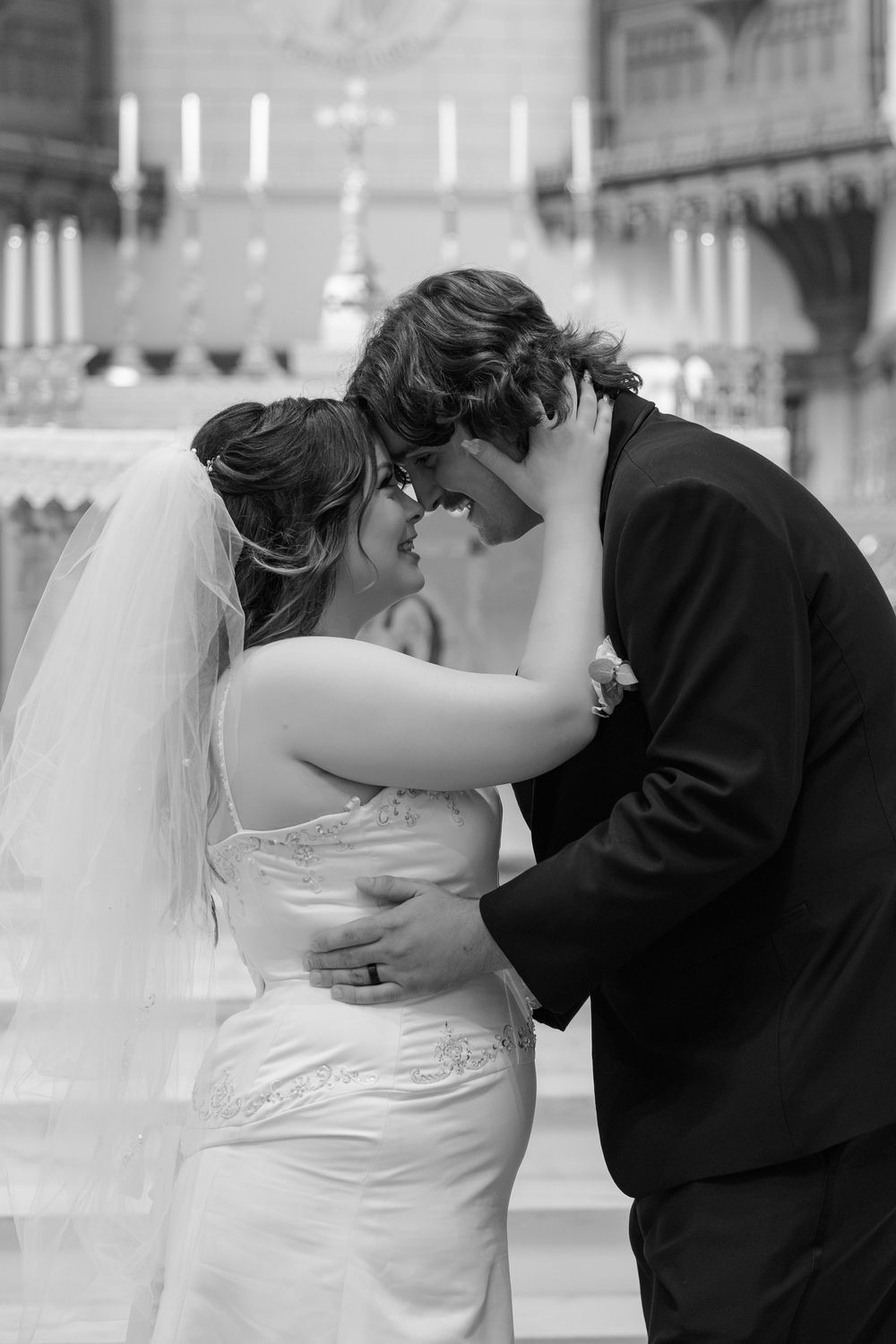 Bride and groom sharing romantic moment at church altar, black and white wedding portrait with candles.