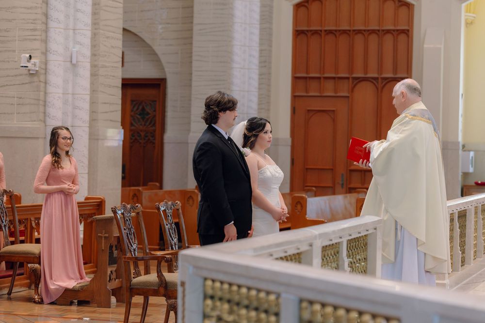 Bride and groom exchange vows with a priest at a church altar, accompanied by a bridesmaid in pink.