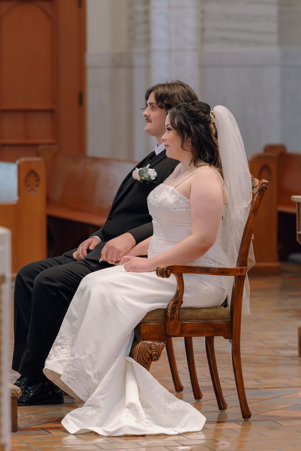 Bride and groom seated together at church altar during wedding ceremony, bride in white gown with veil.