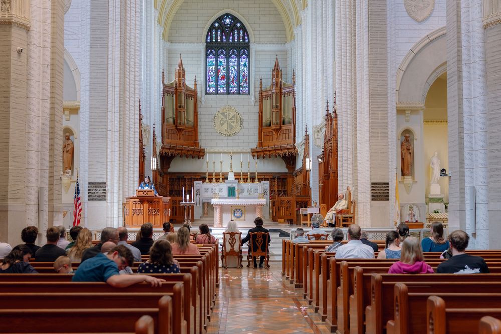 Interior of a grand church with wooden pews, ornate pipe organ, and stained glass windows during a service.
