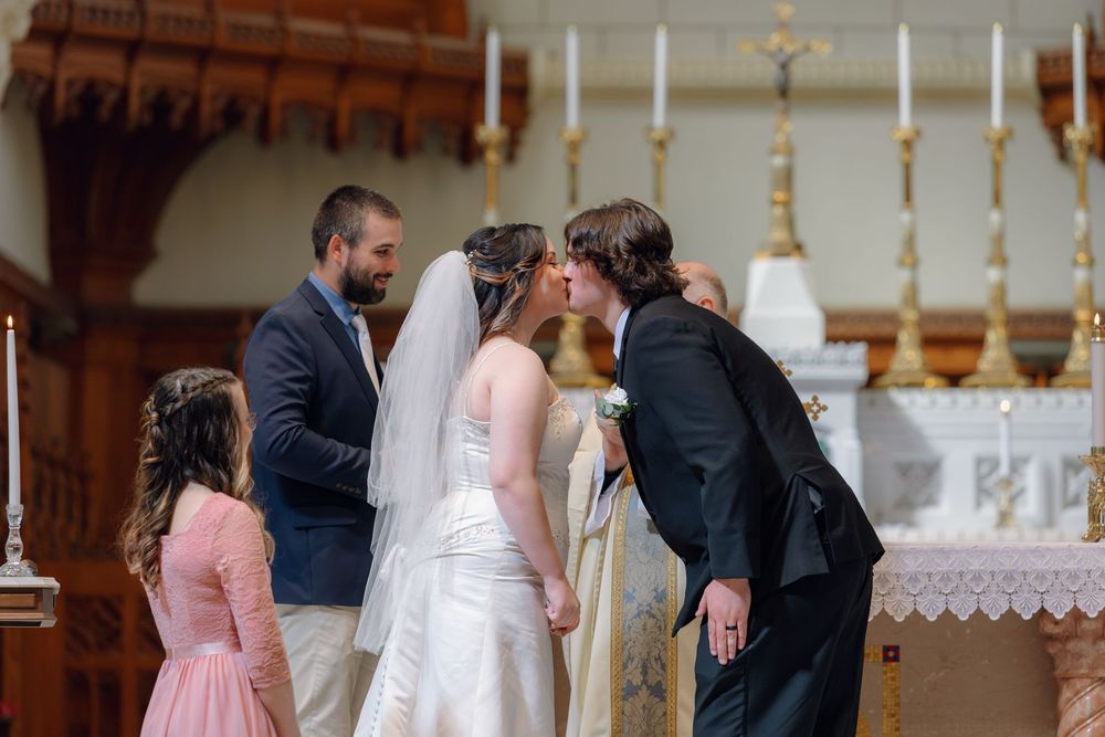Bride and groom share first kiss at church altar during wedding ceremony with guests watching.