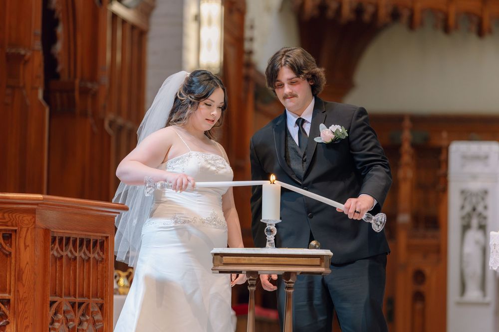 Bride and groom lighting a unity candle together during a church wedding ceremony.