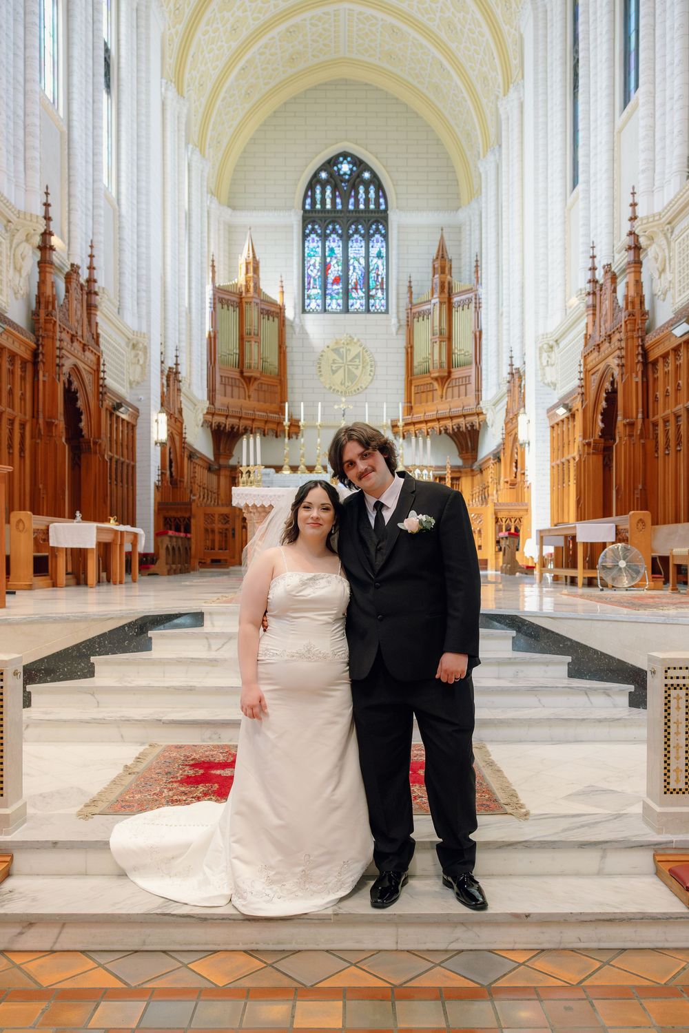 Newlywed couple poses together at church altar steps in stunning cathedral with pipe organ and stained glass.