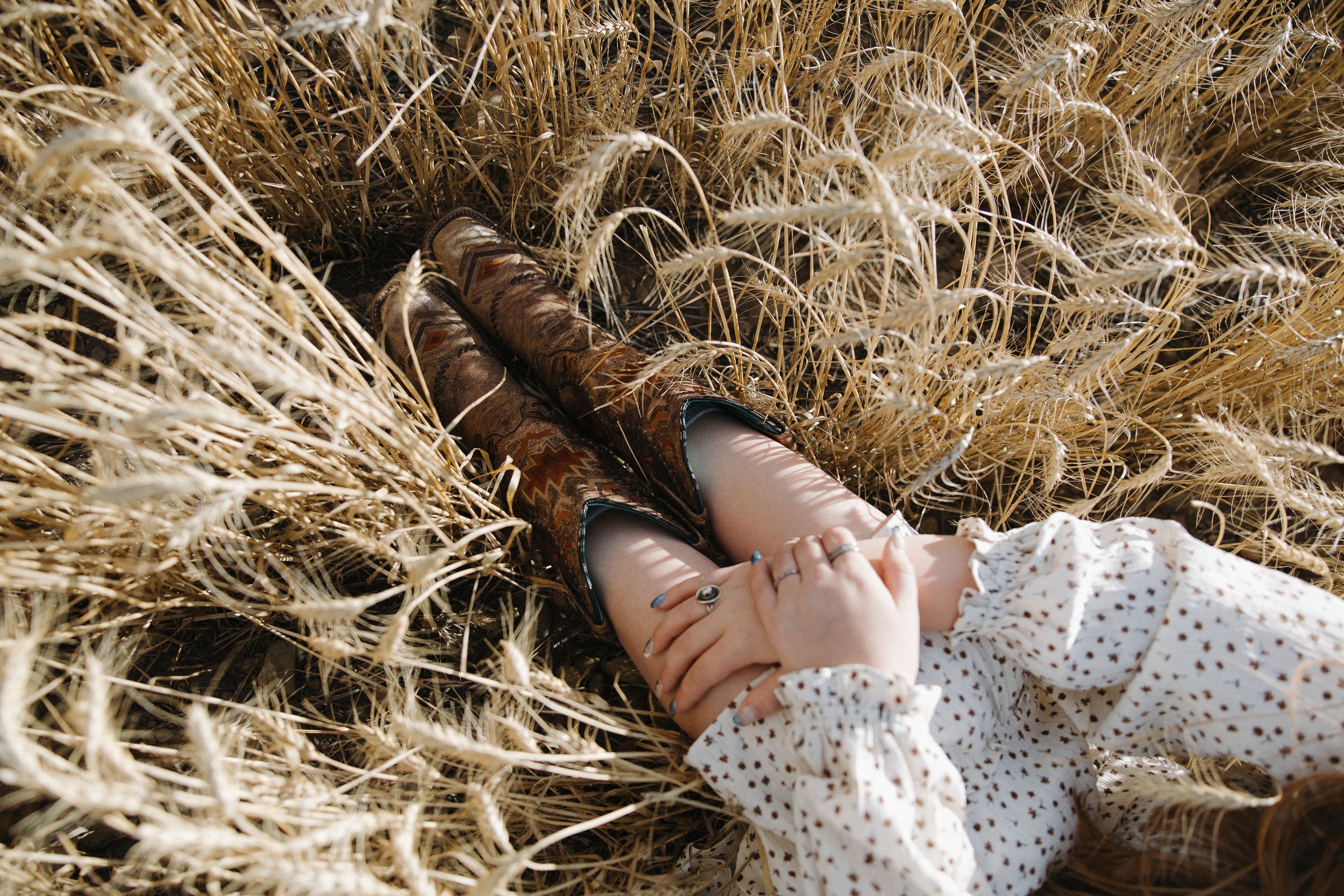 Woman in floral dress lying back in golden wheat field with hands behind her head.