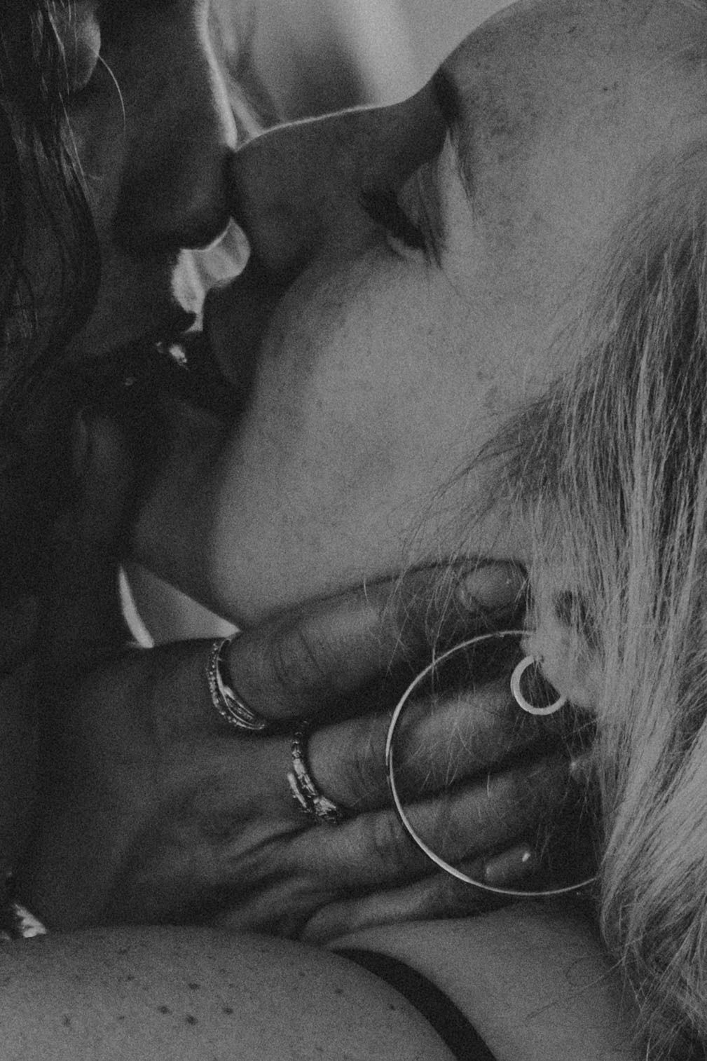 Black and white close-up of two people kissing, one wearing hoop earrings and rings on their fingers.