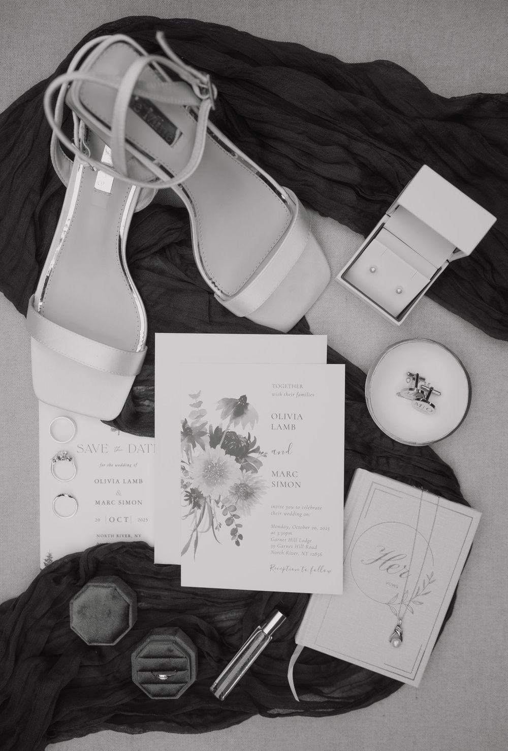 Black and white flat lay of wedding details including heels, invitations, rings, and accessories.