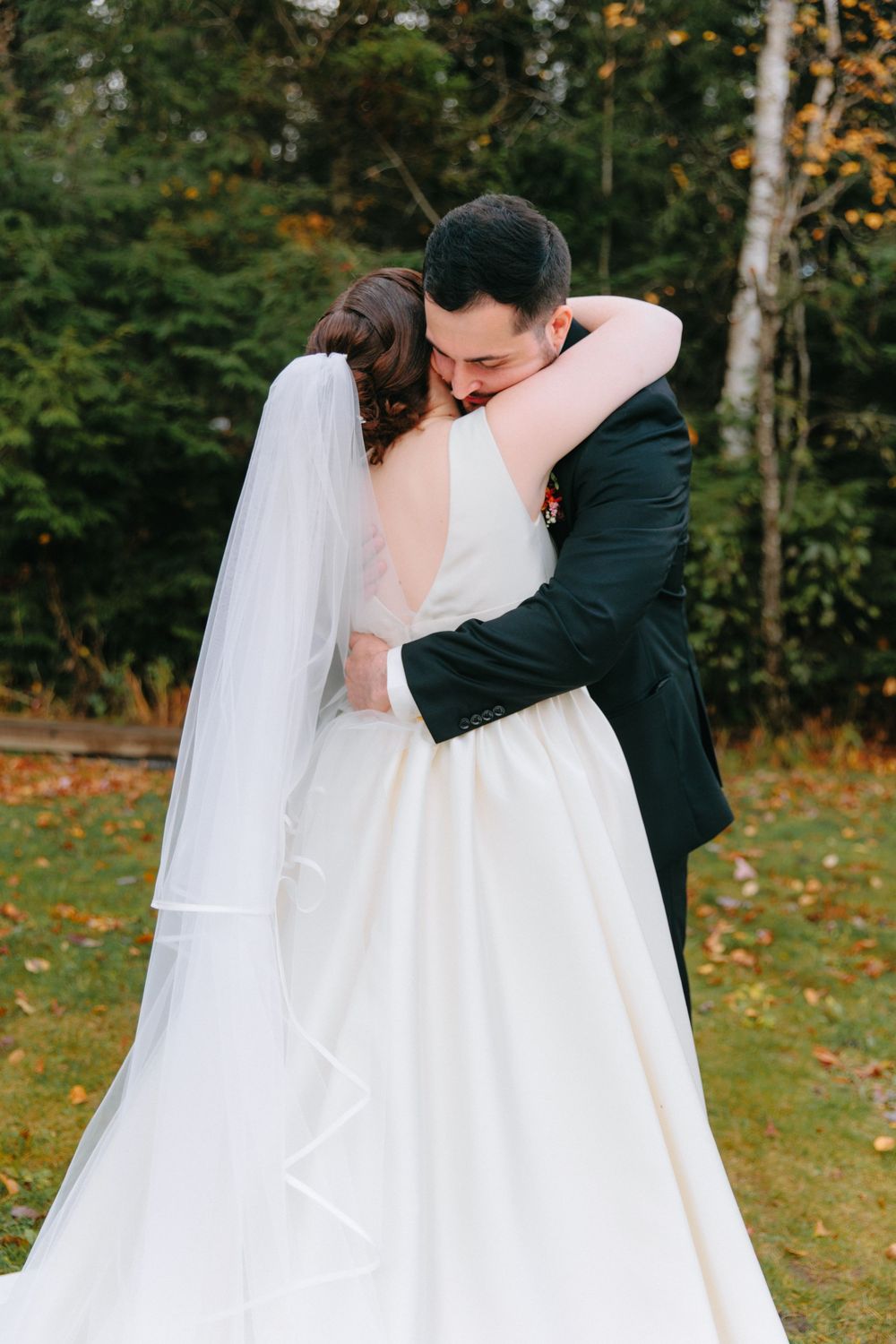 Bride in white gown with long veil embraces groom in dark suit during emotional first look outdoors.