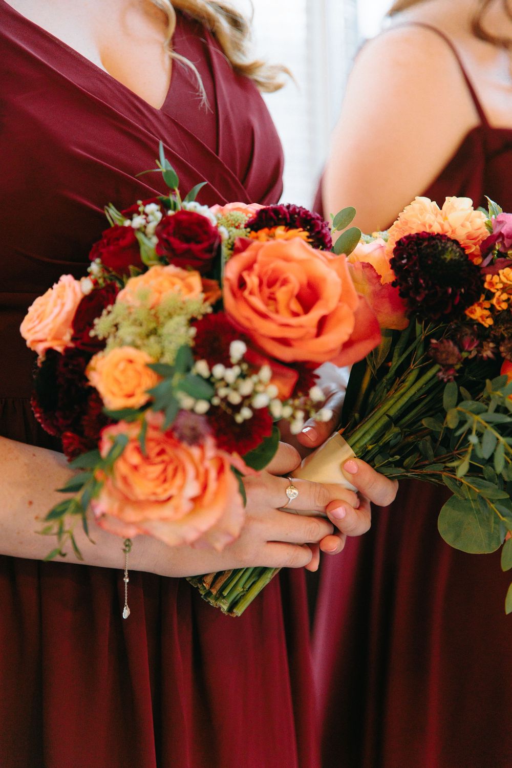 Bridesmaids in burgundy dresses holding vibrant orange and red rose wedding bouquets.