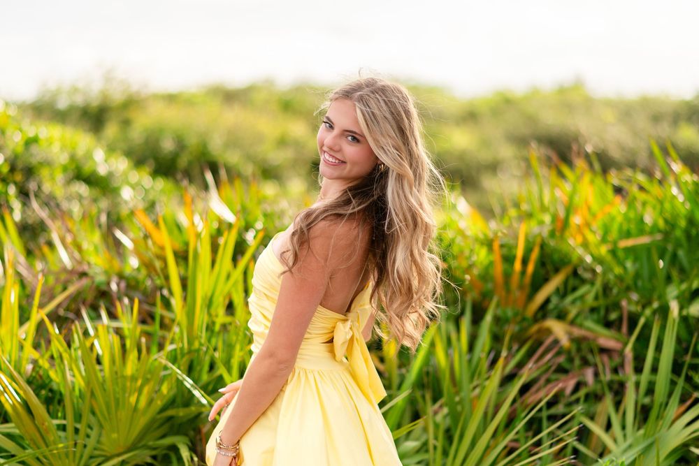 Young woman in yellow dress smiling over shoulder in lush tropical garden.