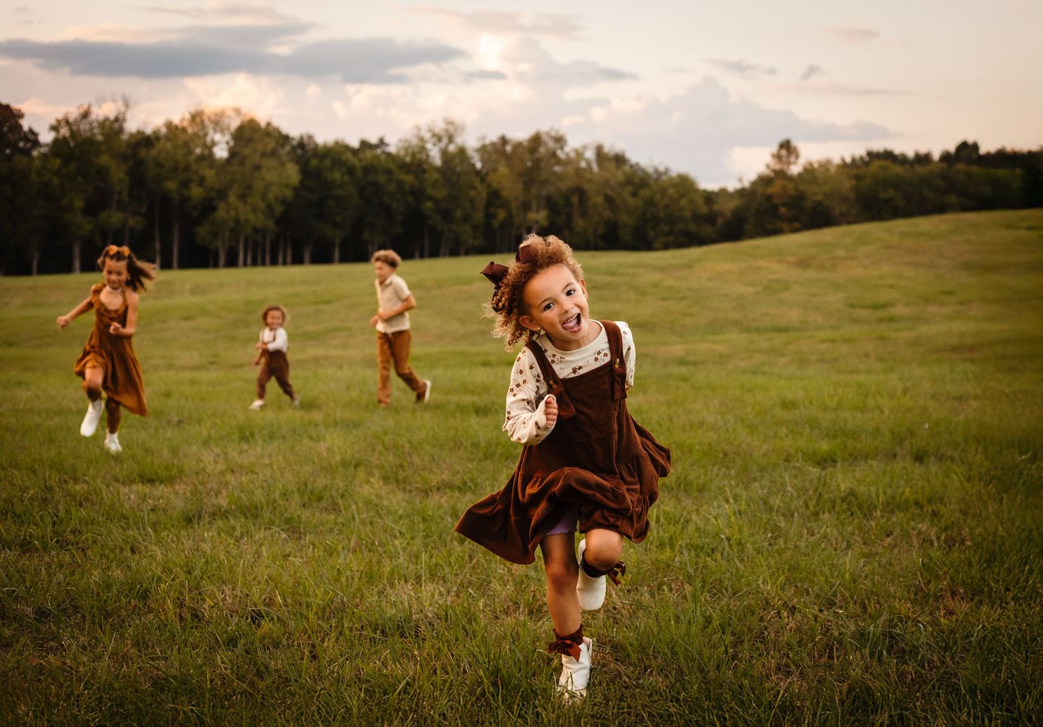 Four adorable siblings dressed in brown corduroy run in a field four their fall family session by Charlottesville baby photographer.