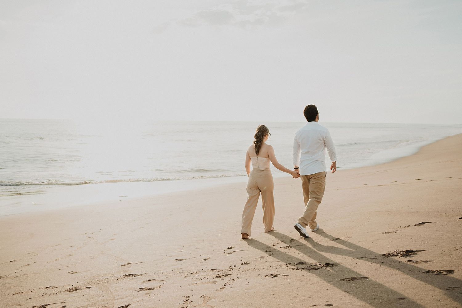 Pareja caminando de la mano por la playa durante una sesión fotográfica al atardecer en Mazatlán.