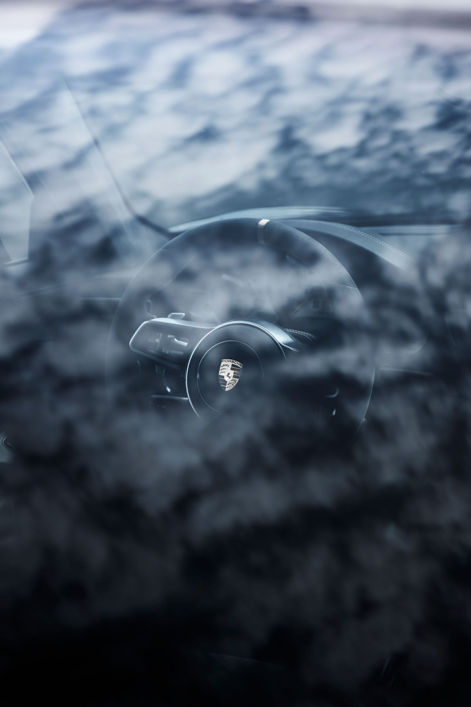 Close-up view through a Porsche windshield revealing the iconic steering wheel logo in a moody, dark atmosphere.
