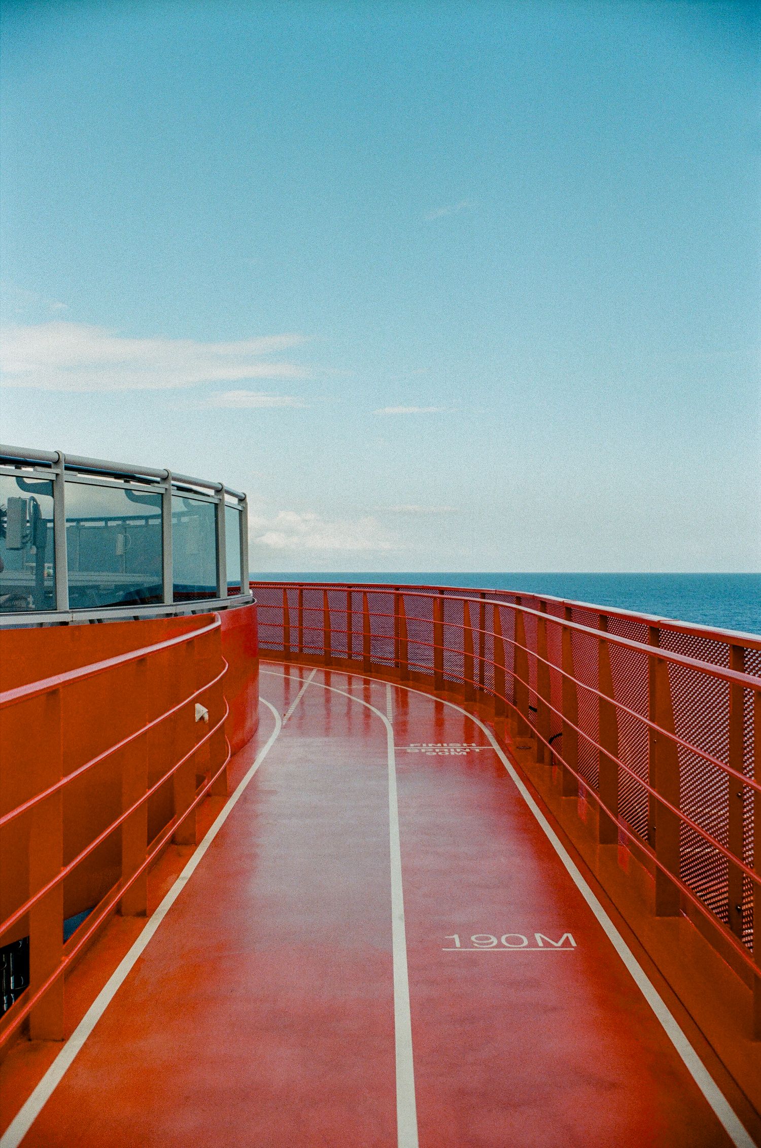 Red outdoor running track on a ferry deck with ocean horizon and blue sky in the background, marked 190M.