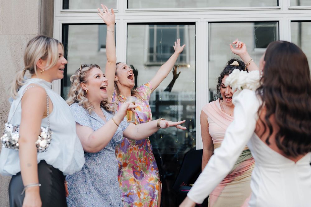 Bridesmaids cheering and raising arms in celebration with bride during outdoor wedding bouquet toss.