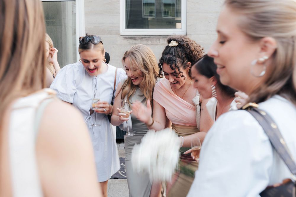 Group of bridesmaids in pink dresses laughing and celebrating together outdoors at a wedding reception.