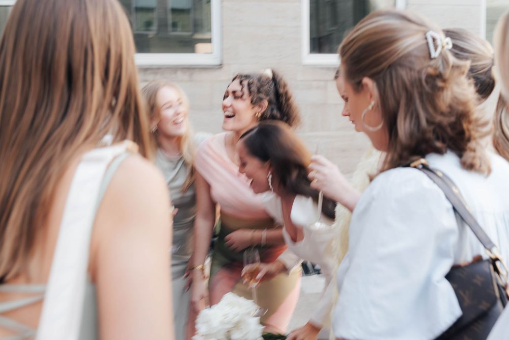Group of women laughing and celebrating outdoors at a wedding or social event on a sunny day.