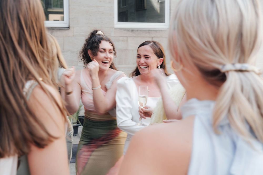 Group of women laughing and socializing outdoors at a party, one holding a champagne glass.